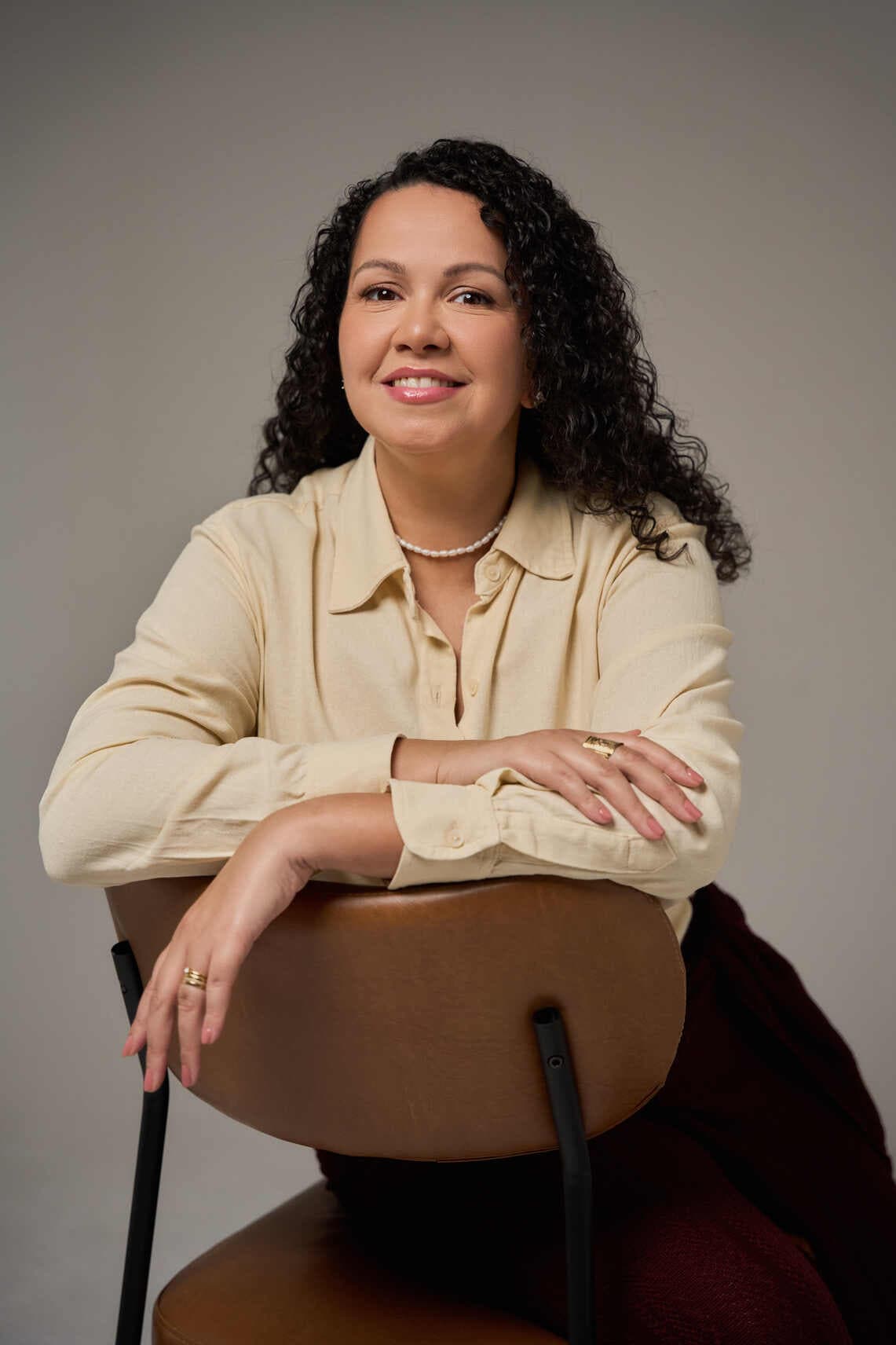 Retrato de Natascha Sam Nelli sentada, apoiada no encosto de uma cadeira